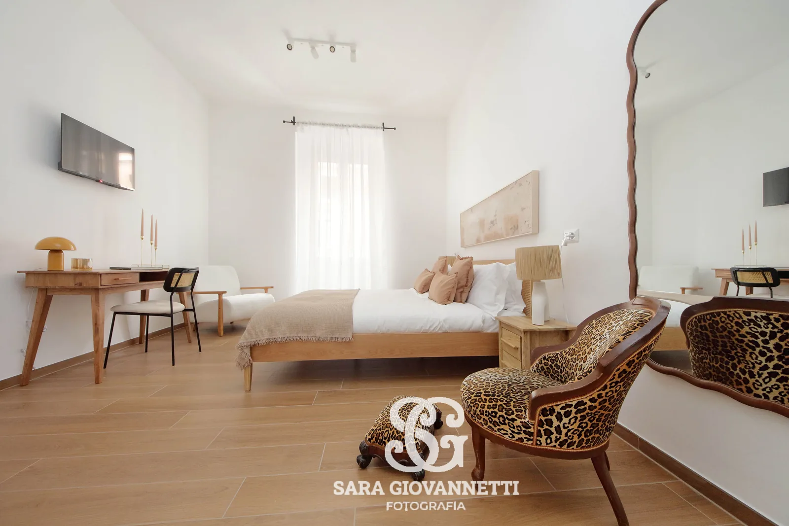 Fotografo Airbnb Roma: camera da letto luminosa con letto in legno, poltrona leopardata e specchio ondulato