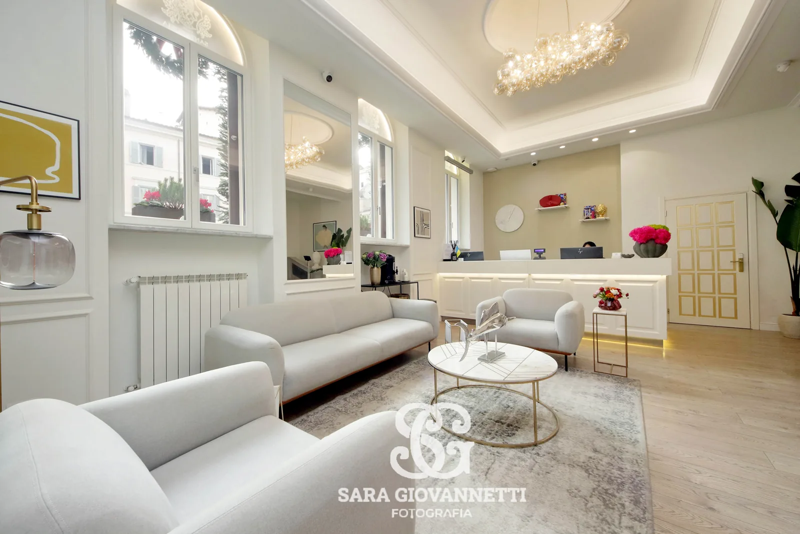 Fotografo Airbnb Roma riprende elegante lobby con reception, divani bianchi, lampadario e finestre ad arco