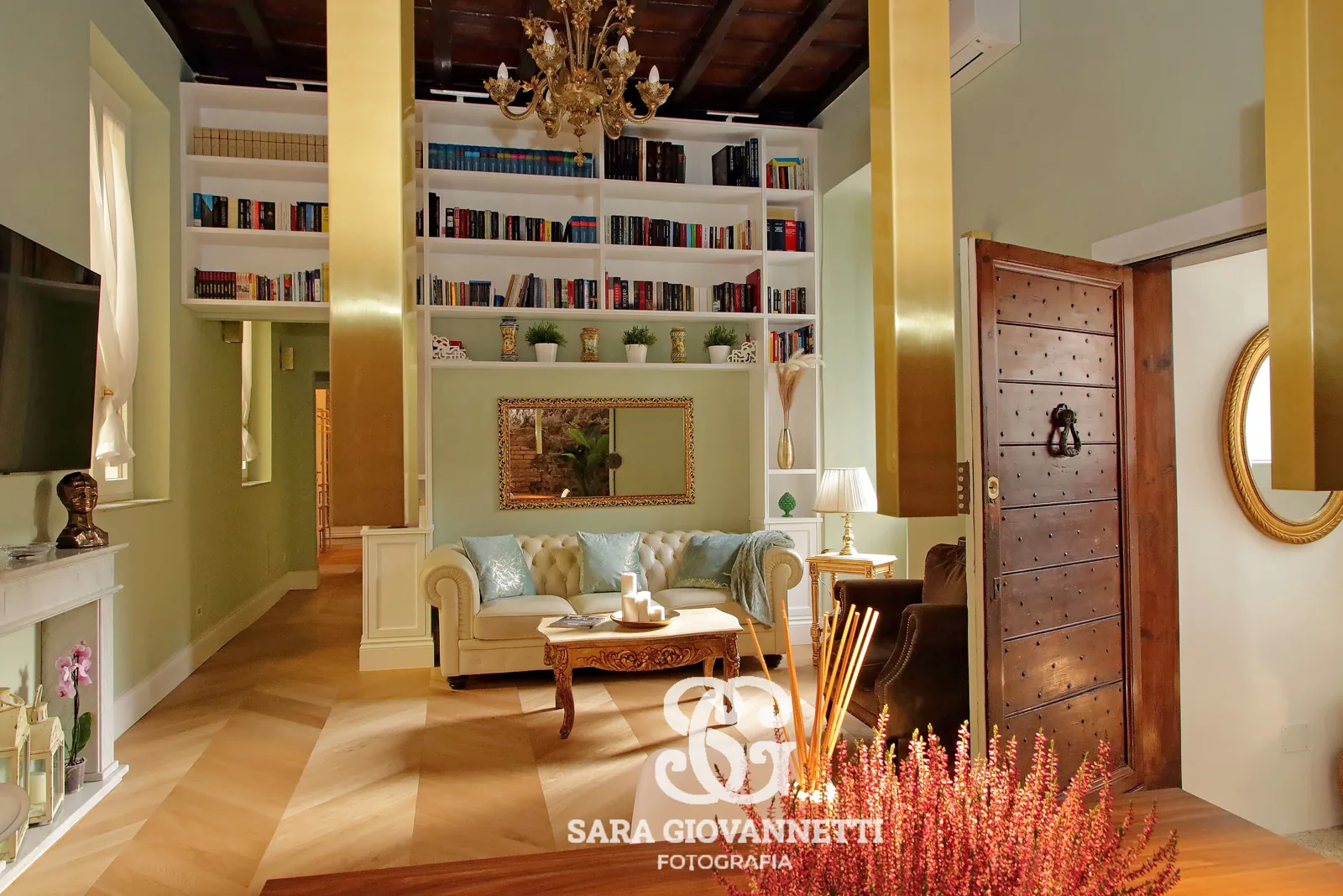 Fotografo Airbnb Roma ritrae elegante soggiorno con libreria a tutta altezza, divano Chesterfield e soffitto in legno