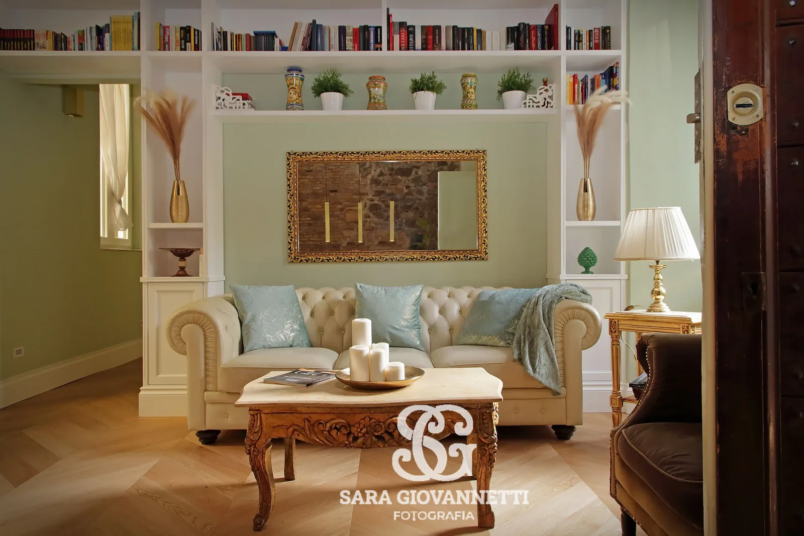 Fotografo Airbnb Roma: soggiorno elegante con divano Chesterfield beige, specchio dorato e libreria a muro in appartamento
